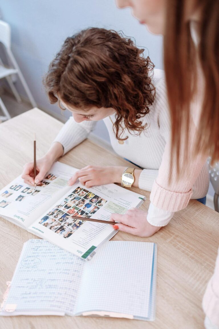 Two women discuss content in a magazine at a table indoors, showcasing teamwork.
